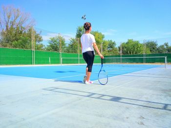 Rear view of woman holding tennis racket while standing on playing field