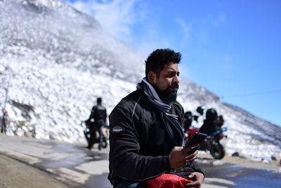 Young man using mobile phone while sitting against snow covered mountain