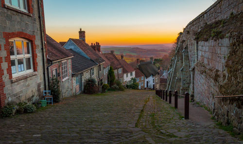 Street amidst buildings against sky during sunset