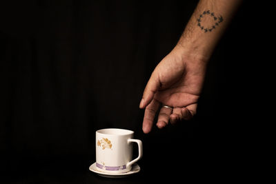 Close-up of hand holding coffee cup against black background