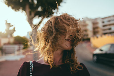 Young woman with hair on face against trees in city