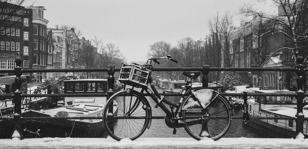 Bicycle parked by railing in city against sky