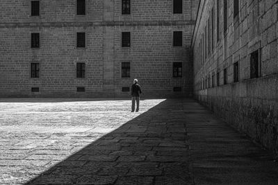 Rear view of man walking on footpath amidst buildings