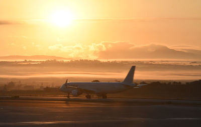 Airplane on runway against sky during sunset