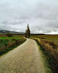 Road passing through field against cloudy sky