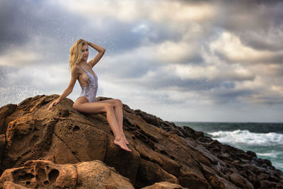 Seductive young woman wearing one piece swimsuit on rocks at beach