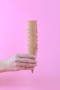 Close-up of hand holding ice cream cones against pink background