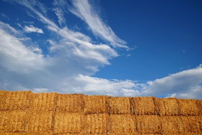 Low angle view of hay bales against cloudy blue sky on sunny day