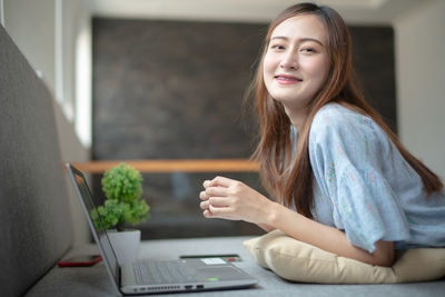 Young woman using smart phone while sitting in laptop