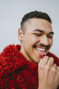 Happy gay man applying lipstick against wall