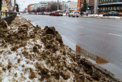 Pile of dirty snow on side of winter city street at cloudy day, close-up with selective focus