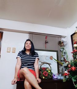 Portrait of young woman sitting on potted plant at home