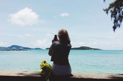 Rear view of mid adult woman sitting by sea against sky