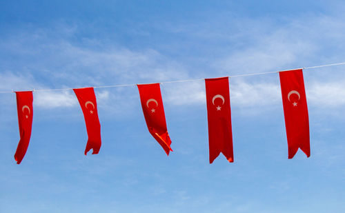 Low angle view of red flags hanging against blue sky
