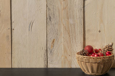 Close-up of pine cones and baubles in basket on table against wall