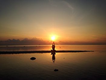 Silhouette boy standing on beach against sky during sunset