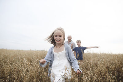 Portrait of happy girl running in an oat field while brother and grandfather following her