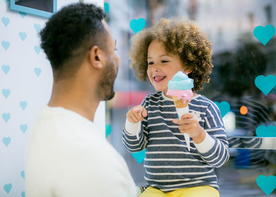 Charming curly ethnic girl holding sweet cone of ice cream playing with black loving father in cafe