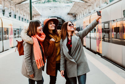 Happy friends taking selfie while standing on station