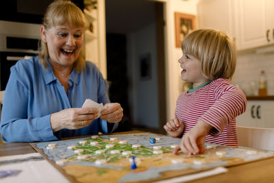 Cheerful grandmother and grandson playing board game at home