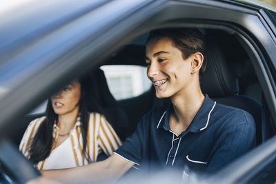 Happy teenage boy learning to drive car with mother