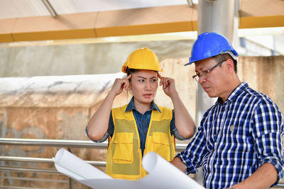 Architects wearing hardhats discussing over blueprint in city