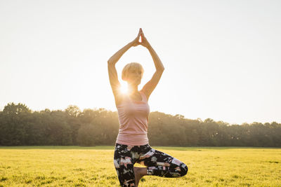 Senior woman doing yoga on rural meadow at sunset