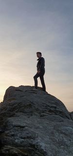 Low angle view of teenage boy standing on rock against sky