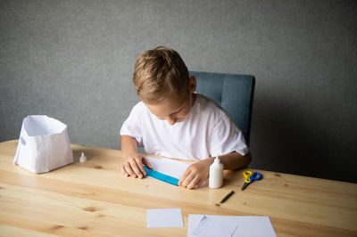 The boy cuts out details from paper. glue the parts together with glue.