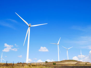 Windmills on field against blue sky