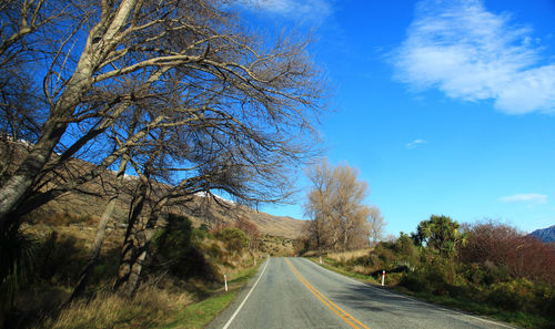 Country road along trees and landscape against blue sky