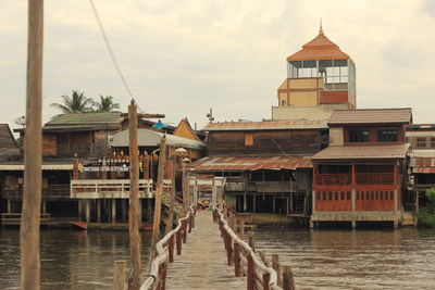 Wooden pier over sea by buildings against sky