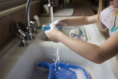 Cropped image of girl washing dishes in kitchen at home