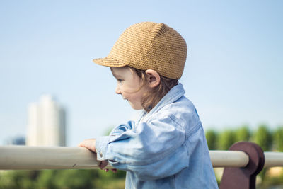 Cute girl looking away by railing against clear sky