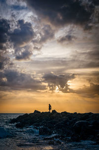 Silhouette woman standing on beach against sky during sunset