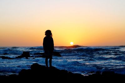 Silhouette woman standing at sea shore against sky during sunset