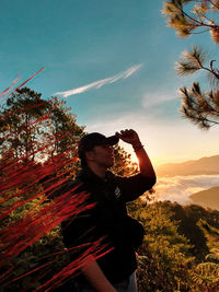 Man photographing by tree against sky
