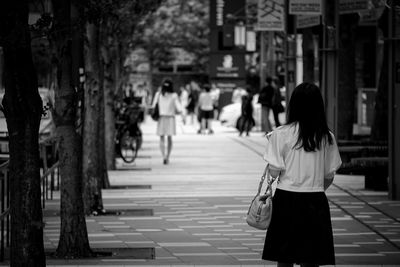 Rear view of woman standing by trees on footpath