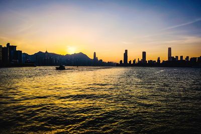 Silhouette buildings by sea against sky during sunset