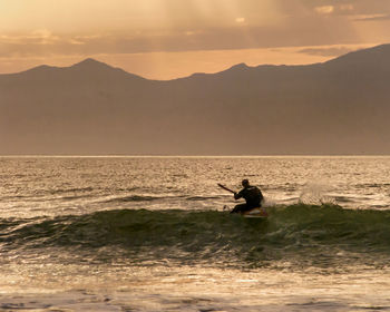 Silhouette man surfing in sea against sky during sunset