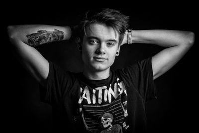 Portrait of young man standing against black background