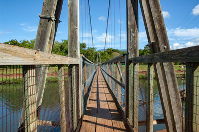 Wooden footbridge amidst trees against sky