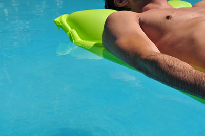 Midsection of man lying on pool raft in swimming pool