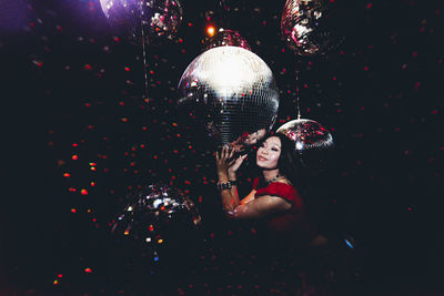 Smiling young woman standing by disco ball in nightclub at night