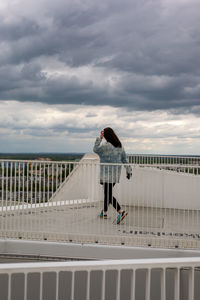 Rear view of woman standing on railing against sky