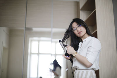 Low angle view of young woman curling hair at home
