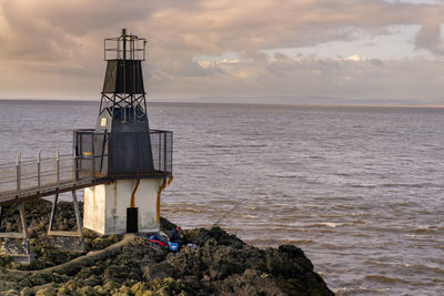 Lighthouse fishing by sea against sky during sunset