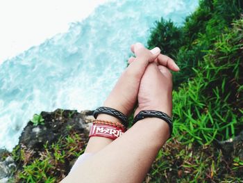 Cropped image of friends wearing bracelets holding hands against plants