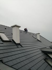 Low angle view of man working on building roof against sky