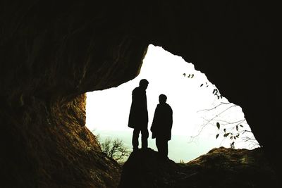 Silhouette men standing in cave against sky